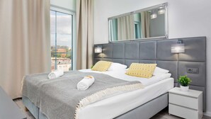 Una habitación de hotel moderna con una cama grande, una mesita de noche, un espejo y vistas a la ciudad.