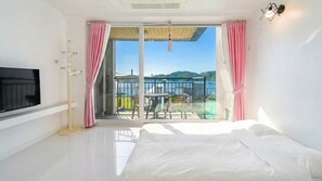 A hotel room with a bed, a TV, a balcony with a table and chairs, and a view of the sea. - Namhae Spring, Summer, Fall, Winter Pet- (Namhae)