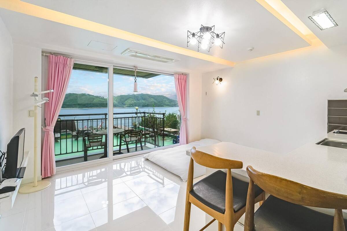 Une cuisine moderne dotée d’un grand îlot central, d’un coin repas avec des chaises et d’une vue sur un lac grâce  à de grandes fenêtres.