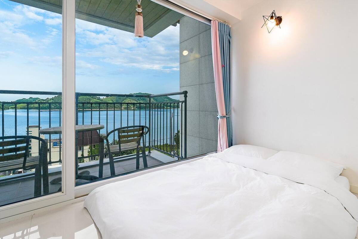 Une chambre avec un grand lit, un balcon avec une table et des chaises, et une vue sur un plan d’eau.