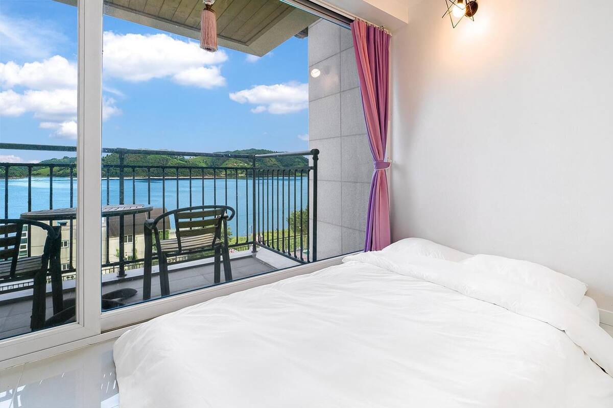 Une chambre avec un balcon donnant sur un lac, un lit et une table avec des chaises.