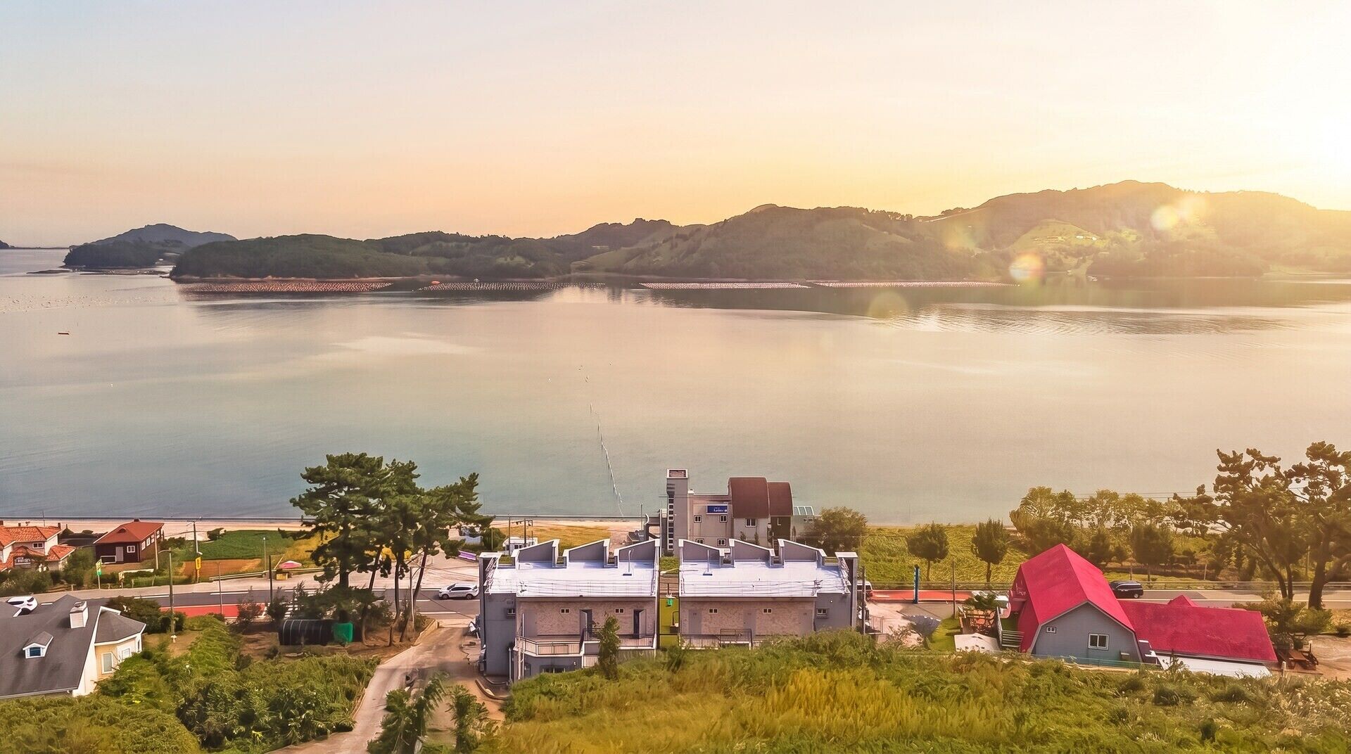 Vista costera con una extensa masa de agua, un puente y un pequeño poblado con edificios y vegetación.