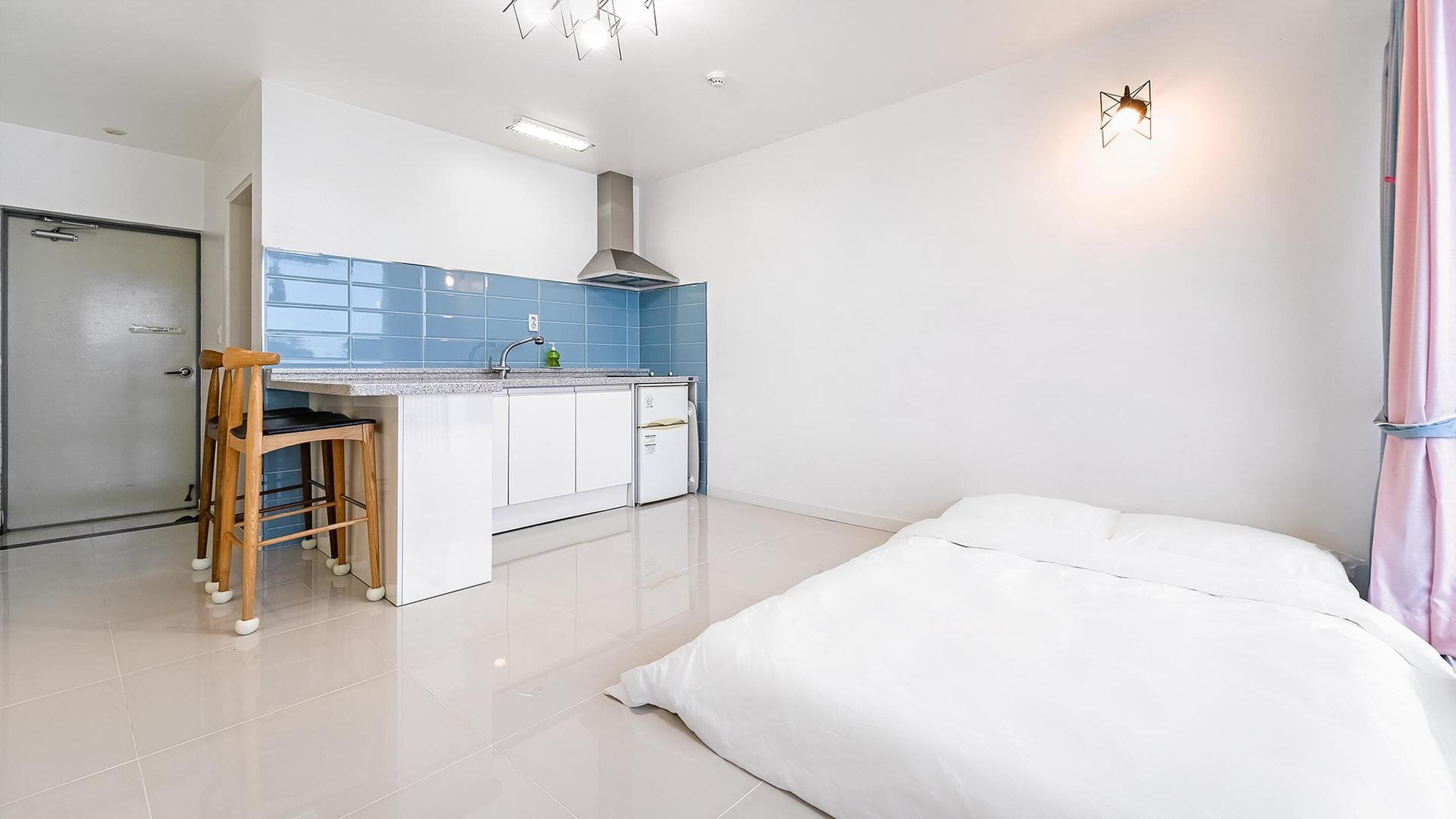 A modern, compact hotel room with a kitchenette, a bed, and a bathroom.