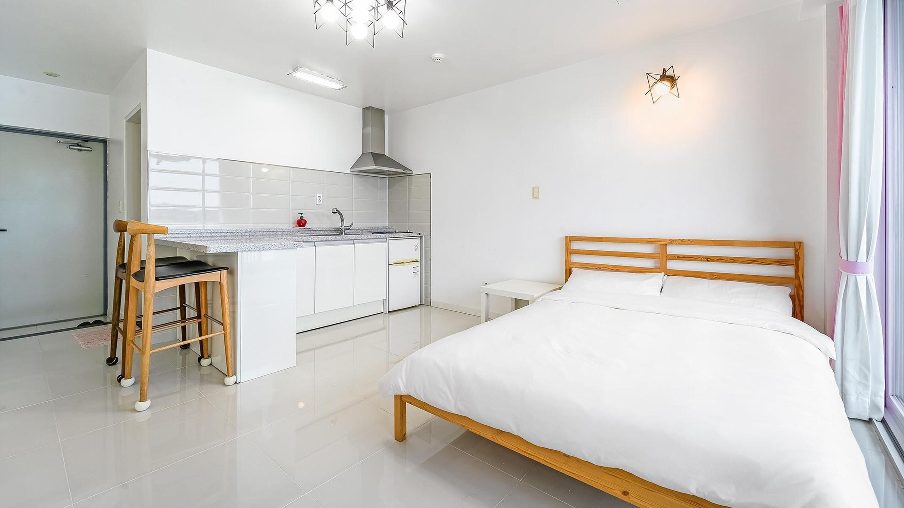 A modern hotel room with a wooden bed, a small kitchenette, and a bathroom.