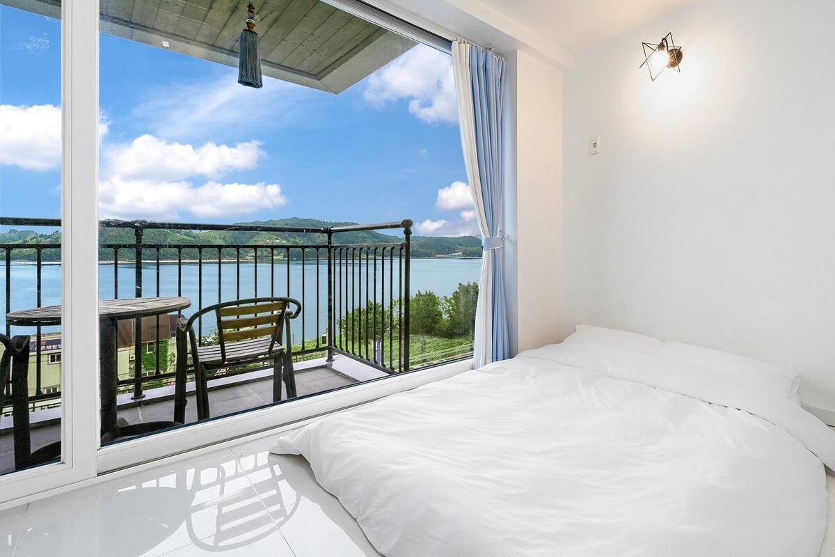 Une chambre avec une grande fenêtre donnant sur un plan d’eau et des collines.