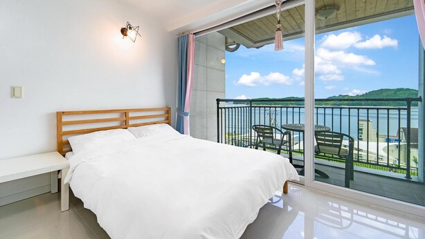 A bedroom with a bed, a bench, a view of the sea, and a balcony with chairs. - Namhae Spring, Summer, Fall, Winter Pet- (Namhae)