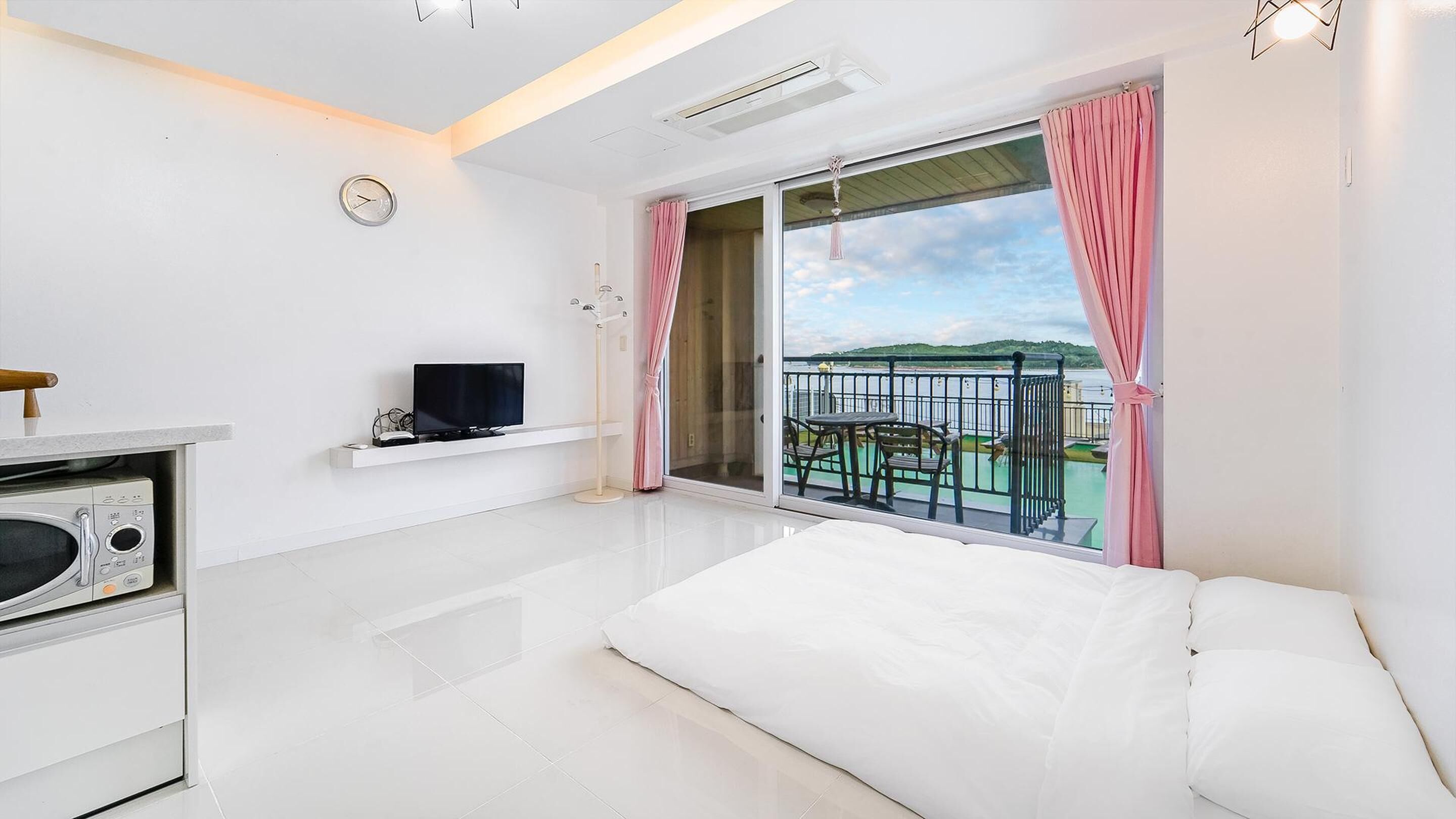 A modern hotel room with a flat-screen TV, a microwave, and a balcony with a view of the sea.
