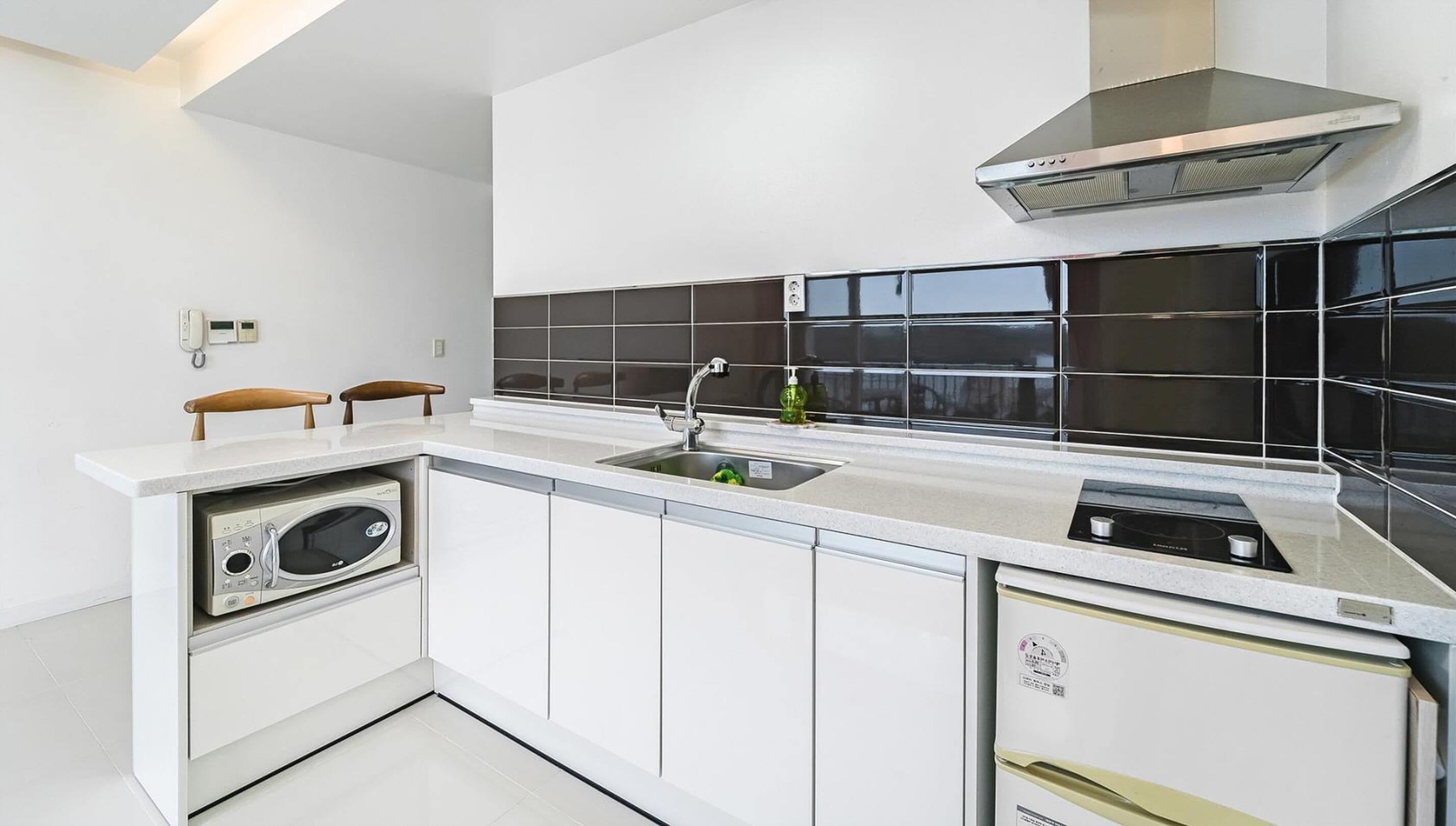 Una cocina moderna con gabinetes blancos, un salpicadero de azulejos negros, horno empotrado y una campana extractora de acero inoxidable.