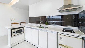 Una cocina moderna con gabinetes blancos, un salpicadero de azulejos negros, horno empotrado y una campana extractora de acero inoxidable.