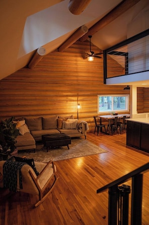 Een gezellig houten blokhut interieur met houten plafond, een bank, een eettafel en een keukenhoek.