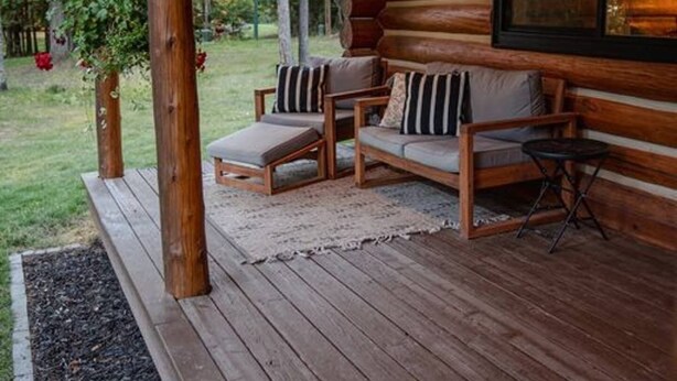 Une cabane en rondins avec une véranda, deux fauteuils confortables, une petite table et un luminaire suspendu.