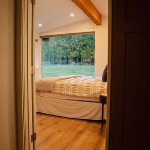 A bedroom with a large window, a bed with a patterned bedspread, and a bedside table.