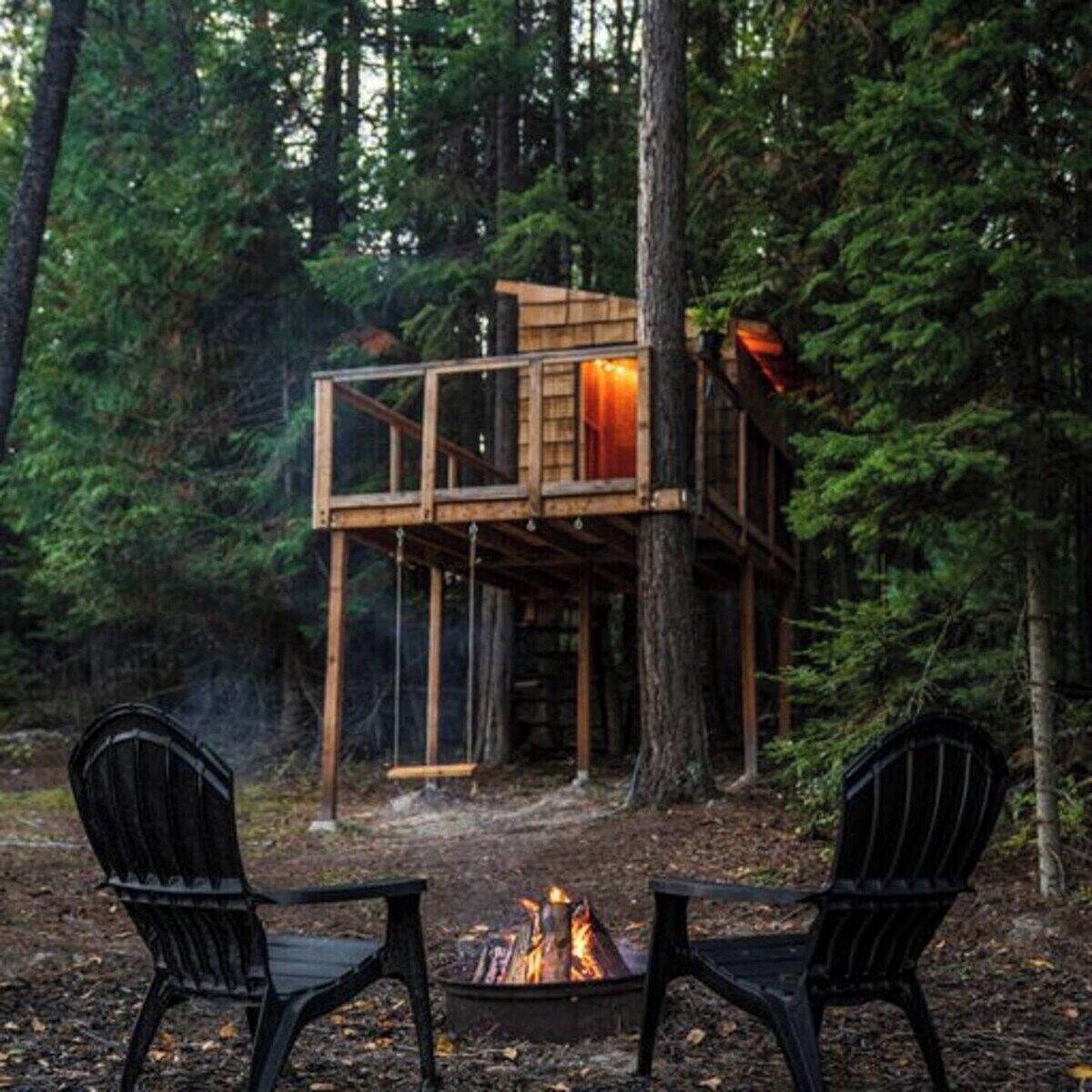 A wooden treehouse with a fire pit and two chairs.
