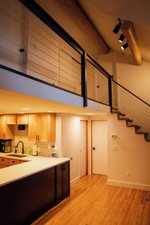 Une cuisine moderne avec des meubles en bois, un îlot central et un escalier menant à un niveau supérieur.