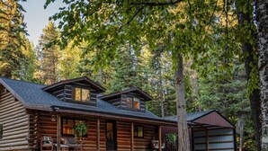 Une cabane en rondins dotée d’un porche couvert, d’un garage et d’une pelouse bien entretenue.