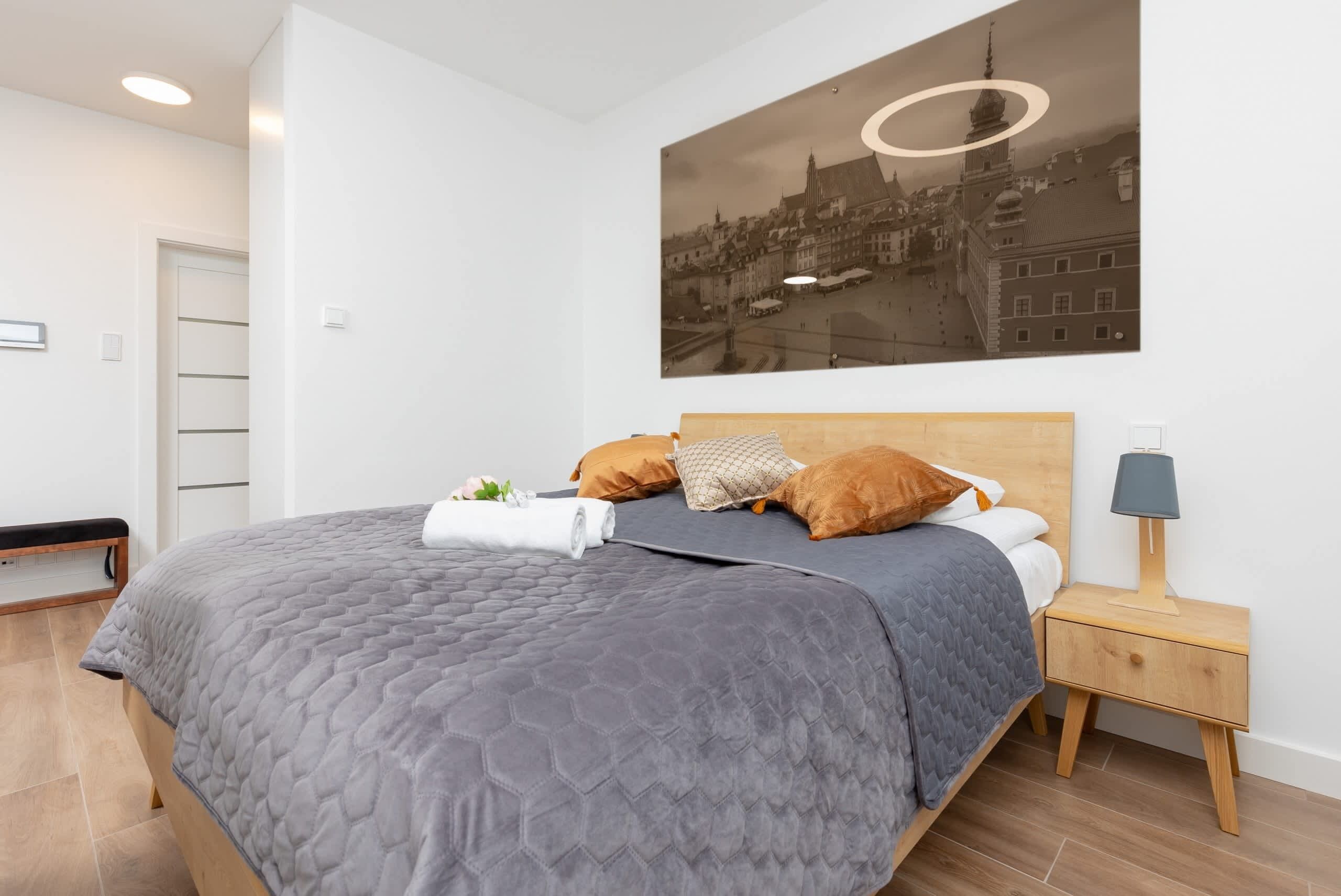 Una camera da letto moderna con un letto grande, un comodino, una lampada e un quadro raffigurante un panorama urbano.