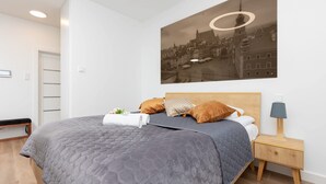 Ein modernes Schlafzimmer mit einem großen Bett, einem Nachttisch, einer Lampe und einem Stadtbild an der Wand.