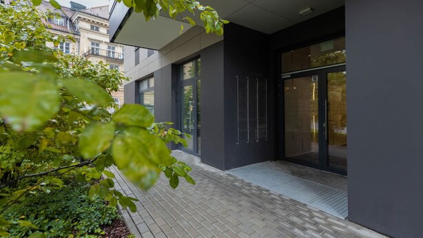 Ein moderner Gebäudeeingang mit Pflasterweg, großen Glastüren und dunkler Fassade.