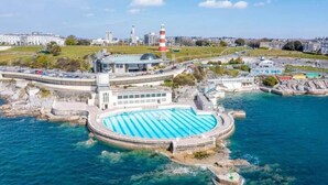 A coastal swimming pool with a lighthouse in the background. - Cozy Coastal Apartment (Plymouth)