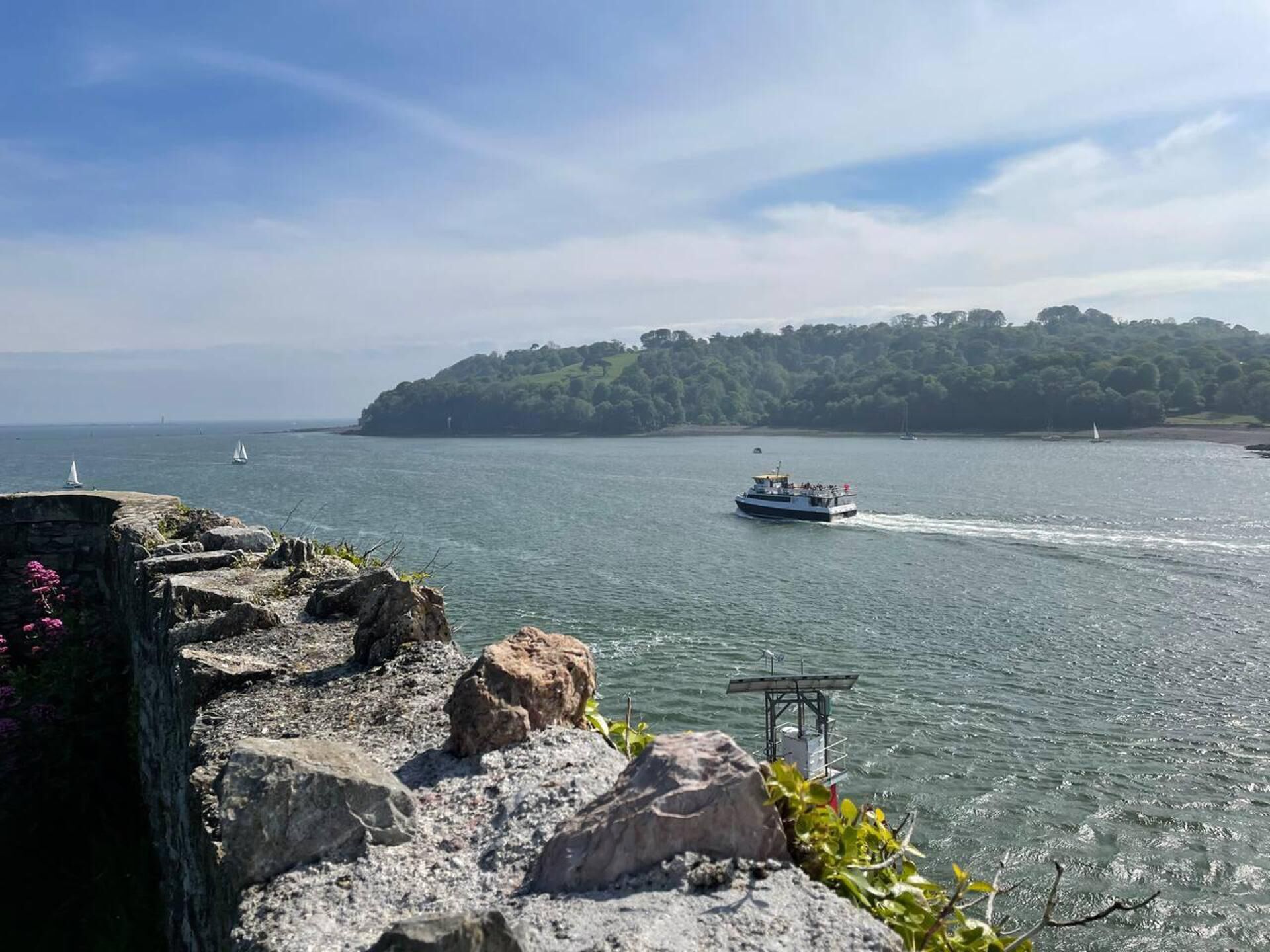 A coastal view with a rocky shoreline, a boat on the water, and a forested island in the distance.