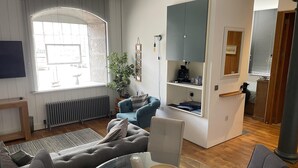 A modern living room with a sofa, a glass coffee table, and a view of the city through large windows. - Cozy Coastal Apartment (Plymouth)