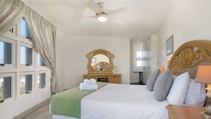 Ein Hotelzimmer mit einem großen Bett, einem Deckenventilator, einer hölzernen Kommode und einem Fenster mit Vorhängen.