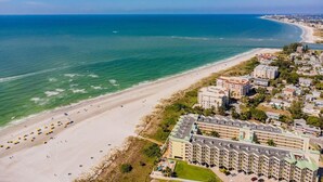 A coastal hotel with multiple buildings, a sandy beach, and a clear view of the ocean.