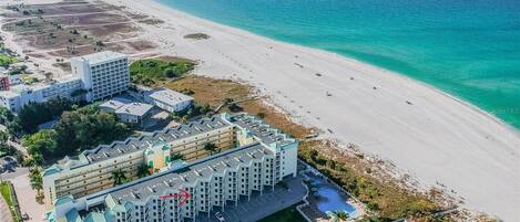 A coastal hotel with multiple buildings, a beach, and a swimming pool.