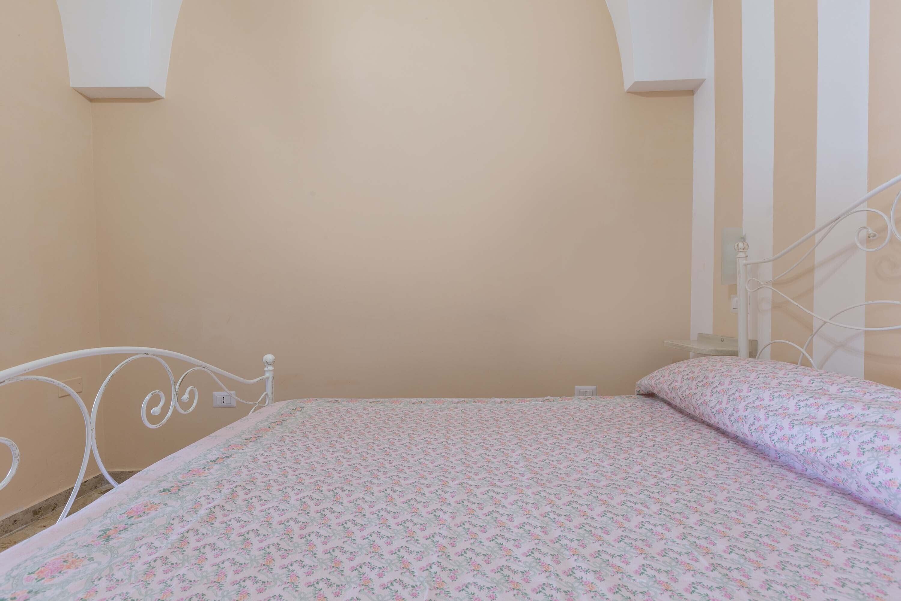 A bedroom with a bed, white metal headboard, and a plain wall.
