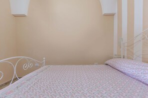 A bedroom with a bed, white metal headboard, and a plain wall.