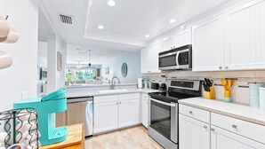 Una cocina moderna con armarios blancos, microondas integrado, estufa y cafetera.