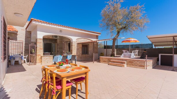 An outdoor patio with a wooden table and chairs, a brick wall, and a tree. - 2842 Villa Colomba - Appartamento A by Barbarhouse (Nardò)