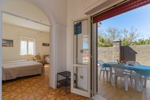 Ein Schlafzimmer mit einem Bett, einem kleinen Tisch und einem Stuhl. Es gibt einen Balkon mit Tisch und Stühlen.