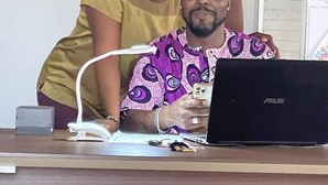 Una persona sentada en un escritorio con una computadora portátil, un teléfono y una taza.