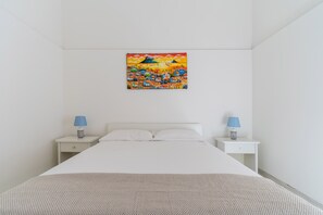 Quarto com uma cama, duas mesas de cabeceira, uma luminária azul em cada uma e um quadro colorido sobre a cama.