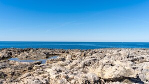 A rocky shoreline with clear blue water and a distant view of the sea.