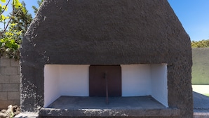 A stone oven with a metal door, surrounded by a concrete base and a brick wall.