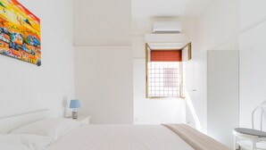 A bedroom with a bed, a nightstand with a lamp, a chair, and a window with blinds.