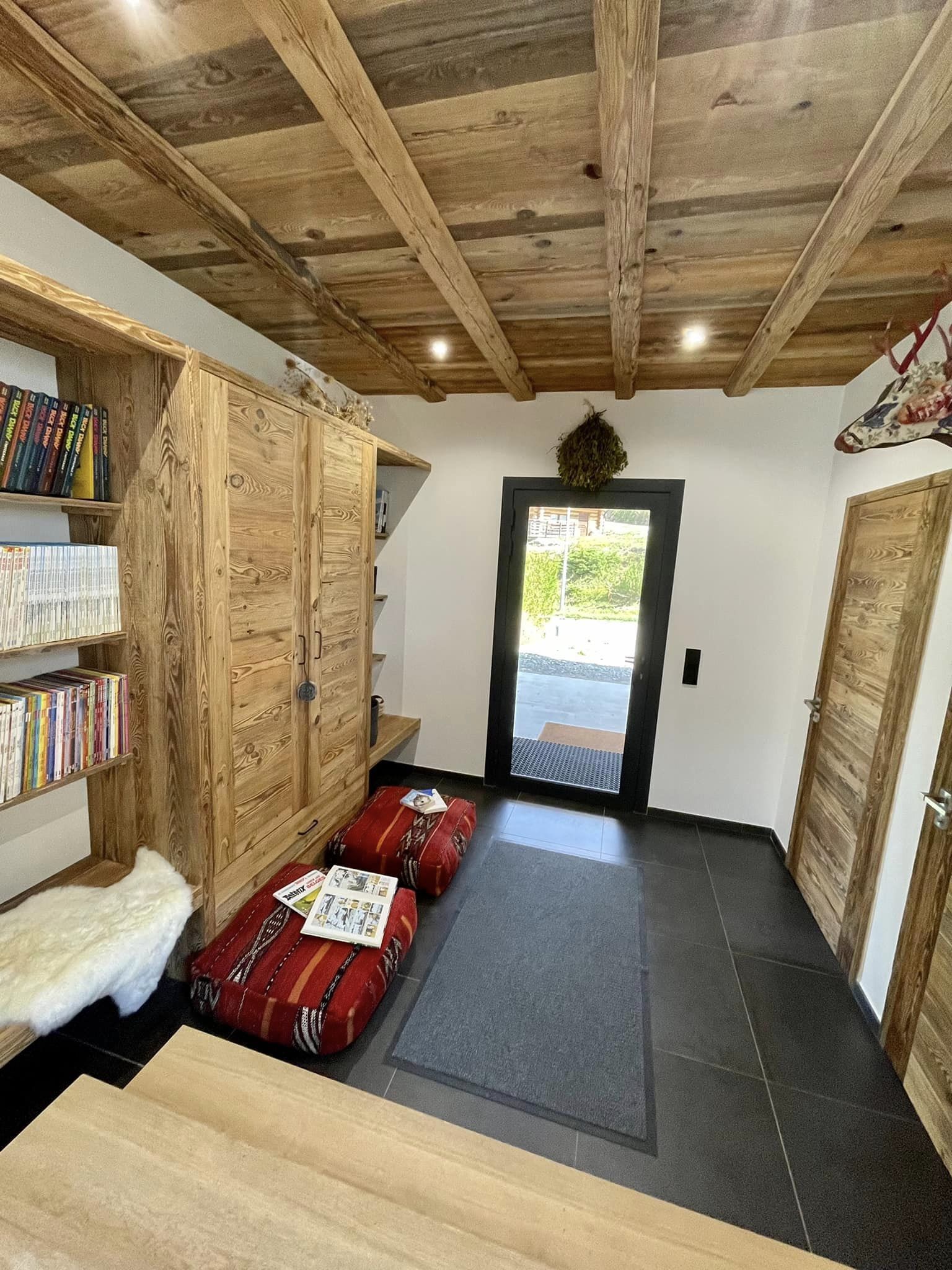 A cozy room with wooden walls and ceiling, a bookshelf, a red sofa, and a small rug.
