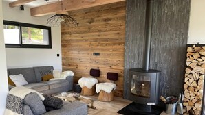 Ein gemütliches Wohnzimmer mit grauem Sofa, Holzelementen, einem Kamin und einer Holzscheinselter.