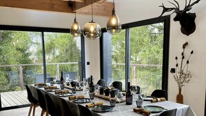Ein Essbereich mit einem langen Tisch, der für eine Mahlzeit gedeckt ist, großen Fenstern und einer Holzzieldecke.