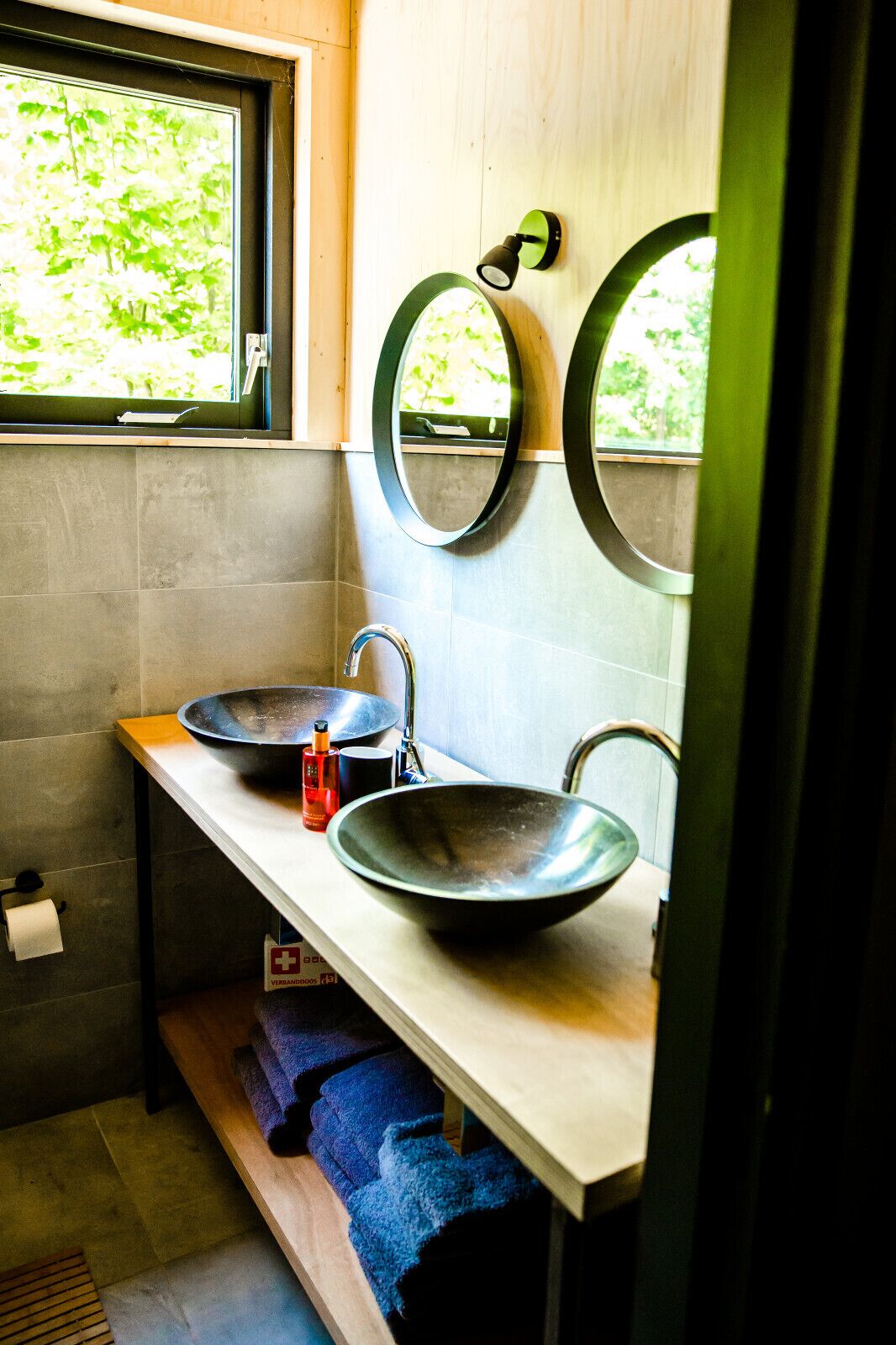 Une salle de bain moderne dotée d’une grande fenêtre, de deux miroirs ronds, d’un lavabo en forme de coupe et d’un porte-serviettes.