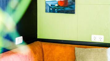 Et værelse med grøn væg, et ur, et blomsterbillede, en brun sofa og en pude med mønster.