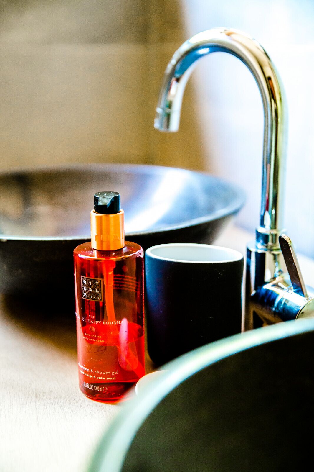 A bathroom sink with a red bottle of shampoo and a blue mug.