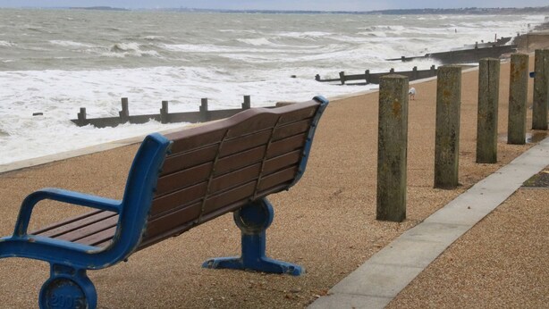 Un banc sur une plage de galets, avec une mer agitée en arrière-plan.