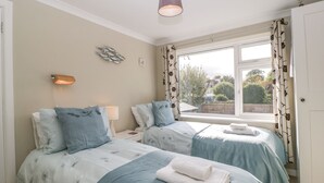 Une chambre avec deux lits, une fenêtre avec des rideaux, un luminaire fixé au mur et un élément décoratif mural.