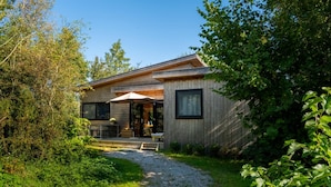 A wooden cabin with a gravel path leading to a patio area with outdoor furniture. - Waterlodge Ljurk in Nes (Nes)