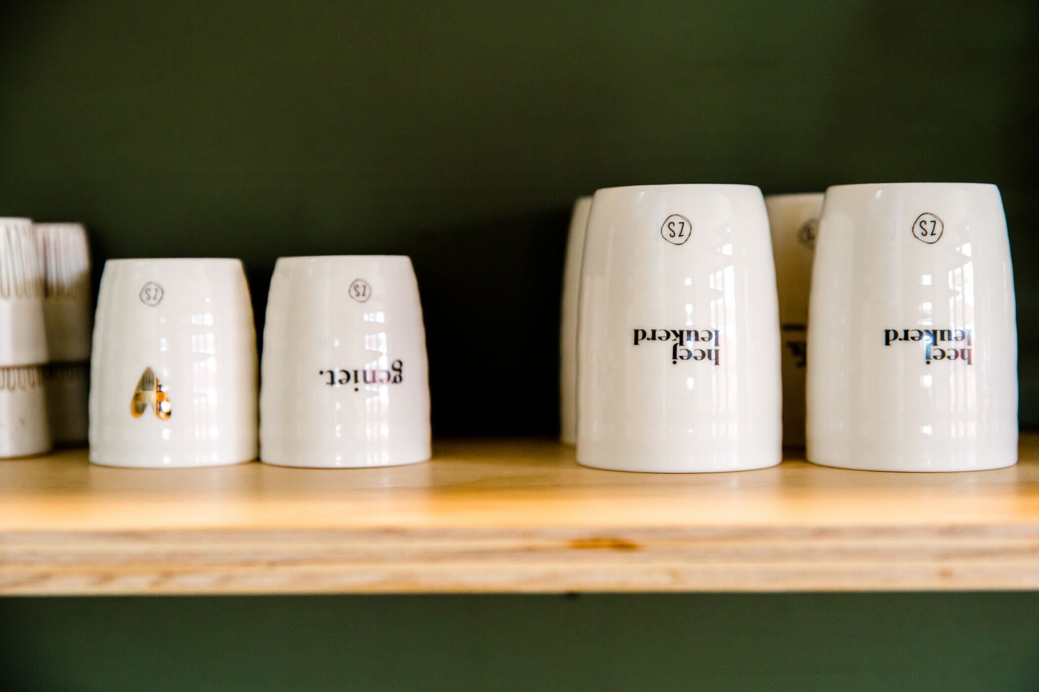 A row of white ceramic mugs with the text "Bergend" and a logo on a shelf.
