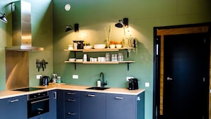 A modern kitchen with a stainless steel range hood, built-in oven, and a double sink. There are wooden shelves above the sink holding dishes and glasses. - Waterlodge Ljurk in Nes (Nes)