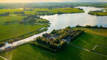 Luftaufnahme eines Flussgrundstücks mit einer zentralen Gebäudegruppe, umgeben von grünen Feldern und einem ruhigen Fluss.